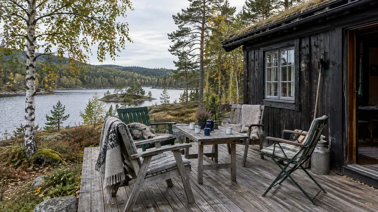 Fire stoler og kaffekopper på terrassen til en trehytte ved vannet.