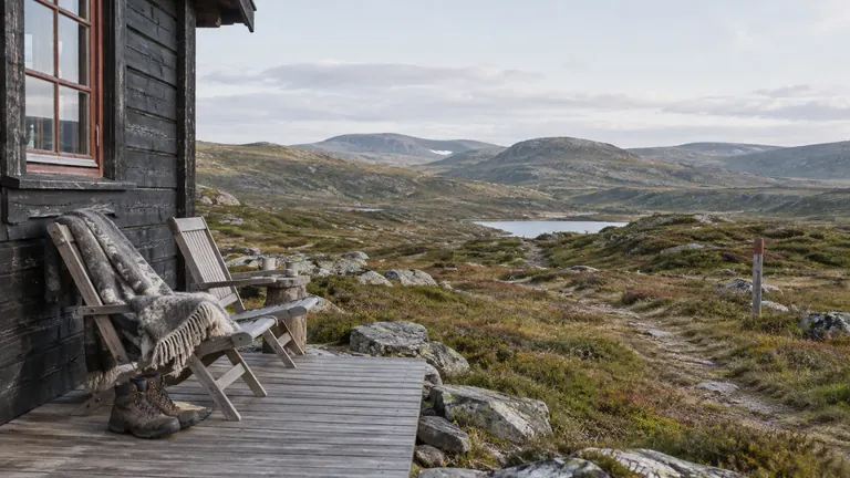 Stoler, ullpledd og turstøvler på en hytteterrasse med utsikt mot fjellet.