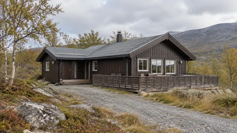 Romslig brun firmahytte med terrasse i et høstlig fjellandskap.