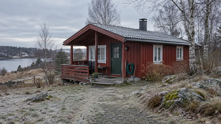 Rød hytte med lukkede vinduer og utemøbler under tak en frostkald høstdag.